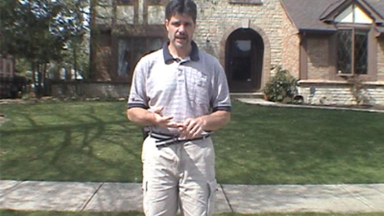 A man standing on lawn with a house in the background.