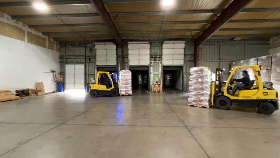 Two forklifts with loaded pallets of seed in a warehouse