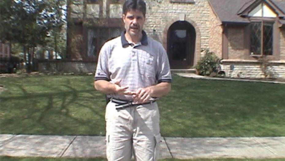 A man standing on lawn with a house in the background.