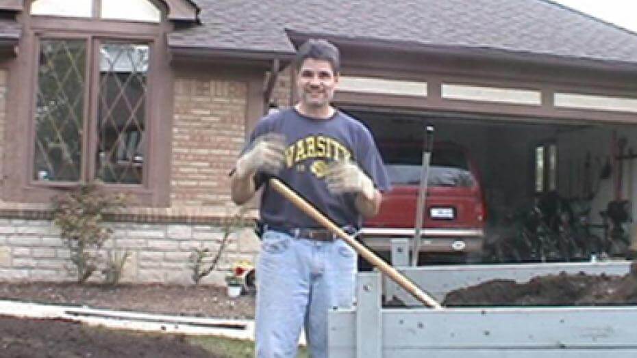 Person standing on a patch of dirt in front of a house.