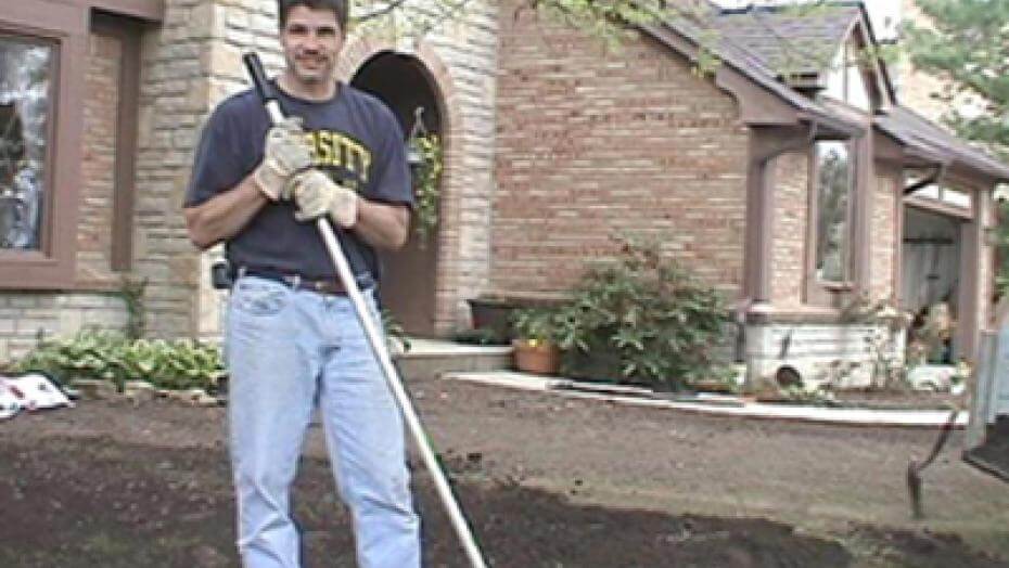 Person standing on a patch of dirt in front of a house.