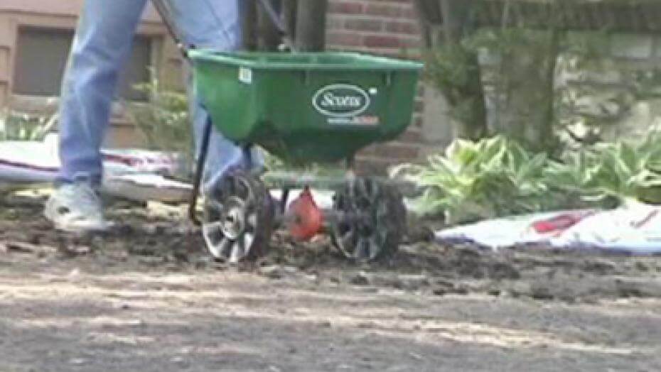 A seed spreader being used on dirt.